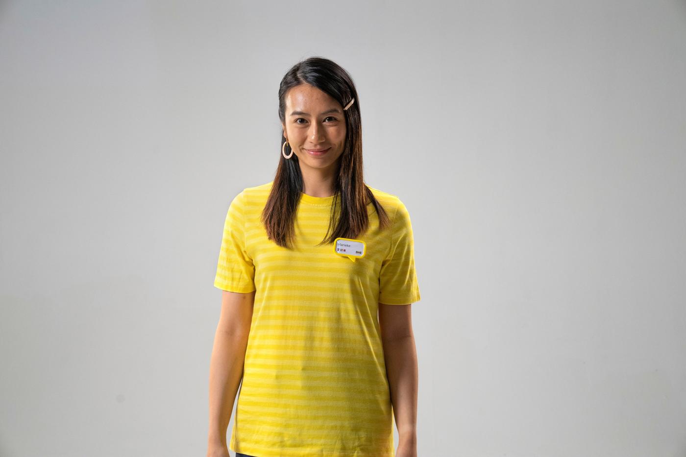 A young person smiles at the camera. She is wearing a yellow striped t-shirt.