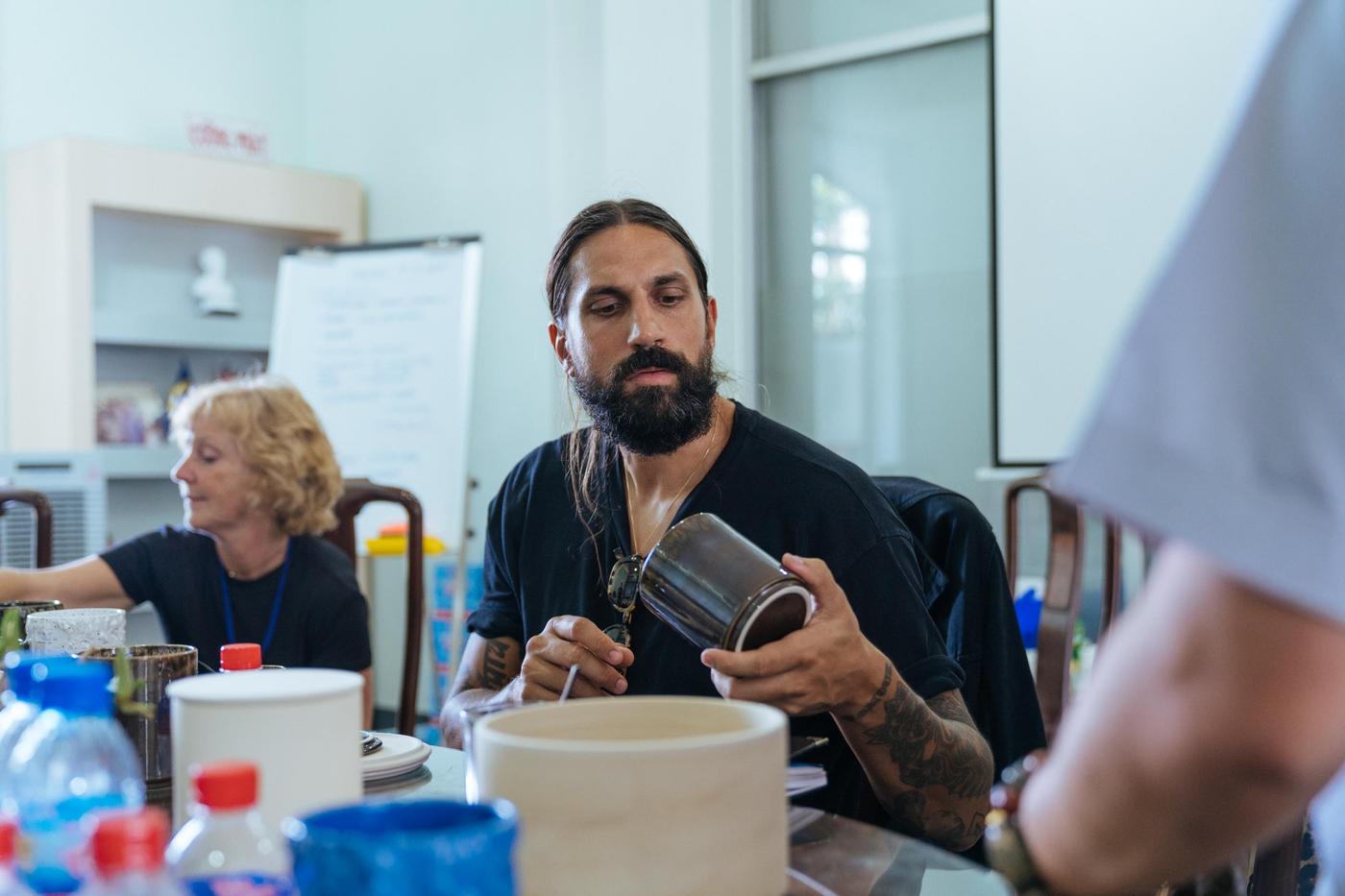 A man looks at a ceramic container. There is a lady working in the background.