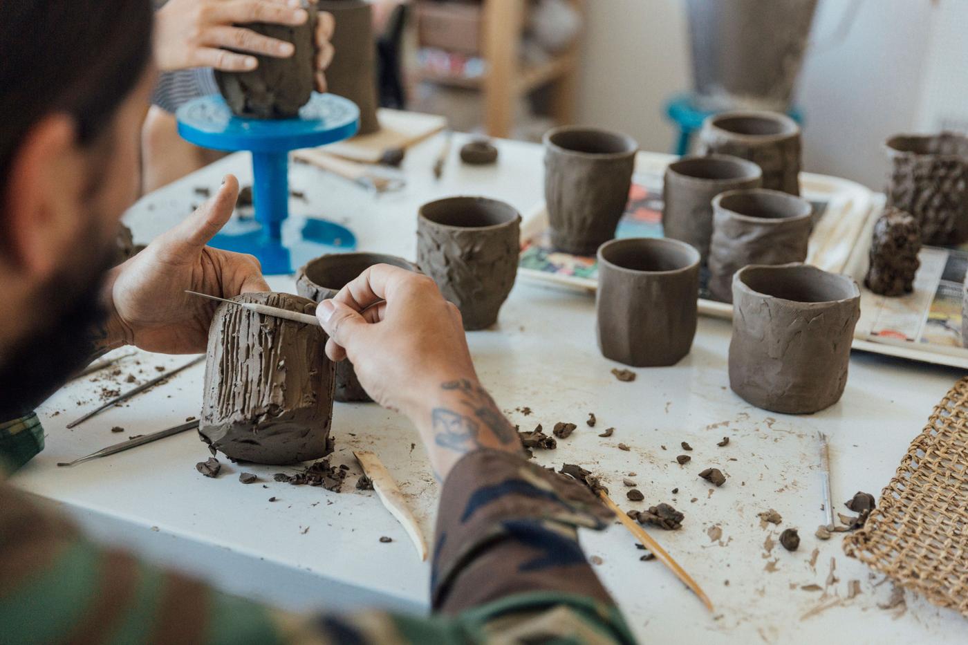 View of a man moulding a shape with brown clay.