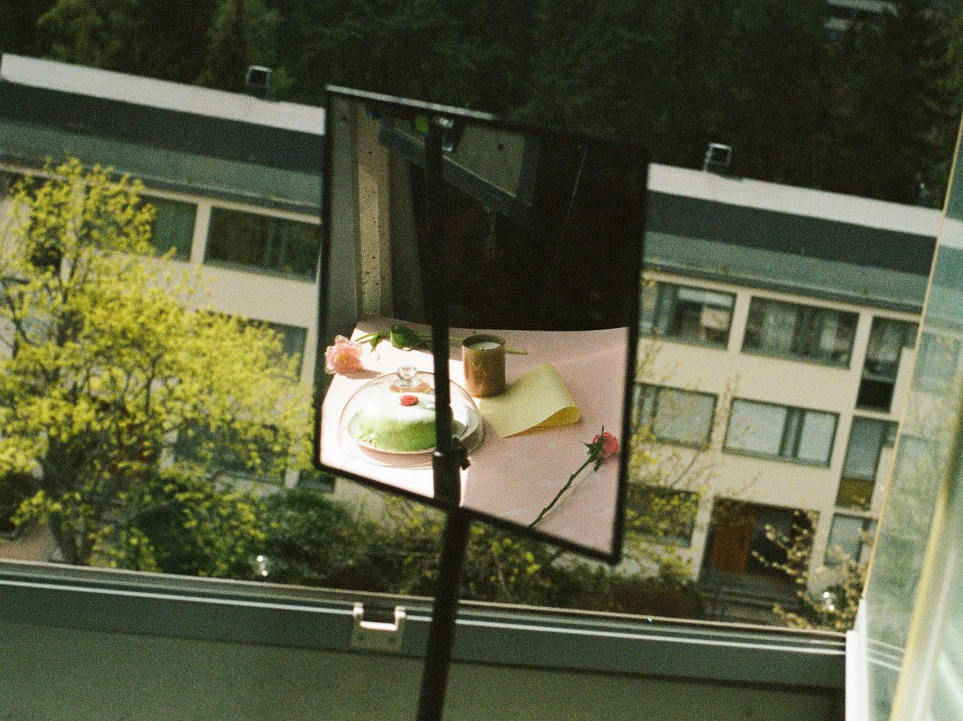 A mirror in front of a window reflects a table with cake and a candle.