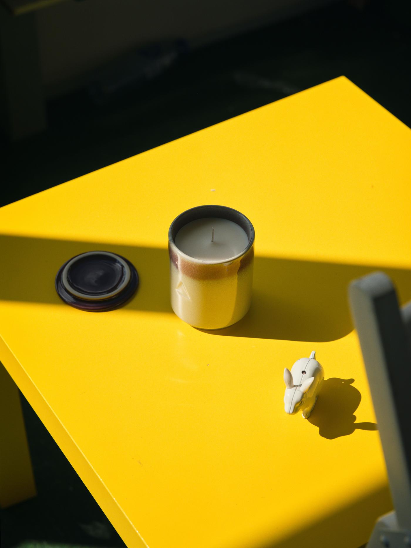 An unlit candle in the shadow sits on a yellow table.