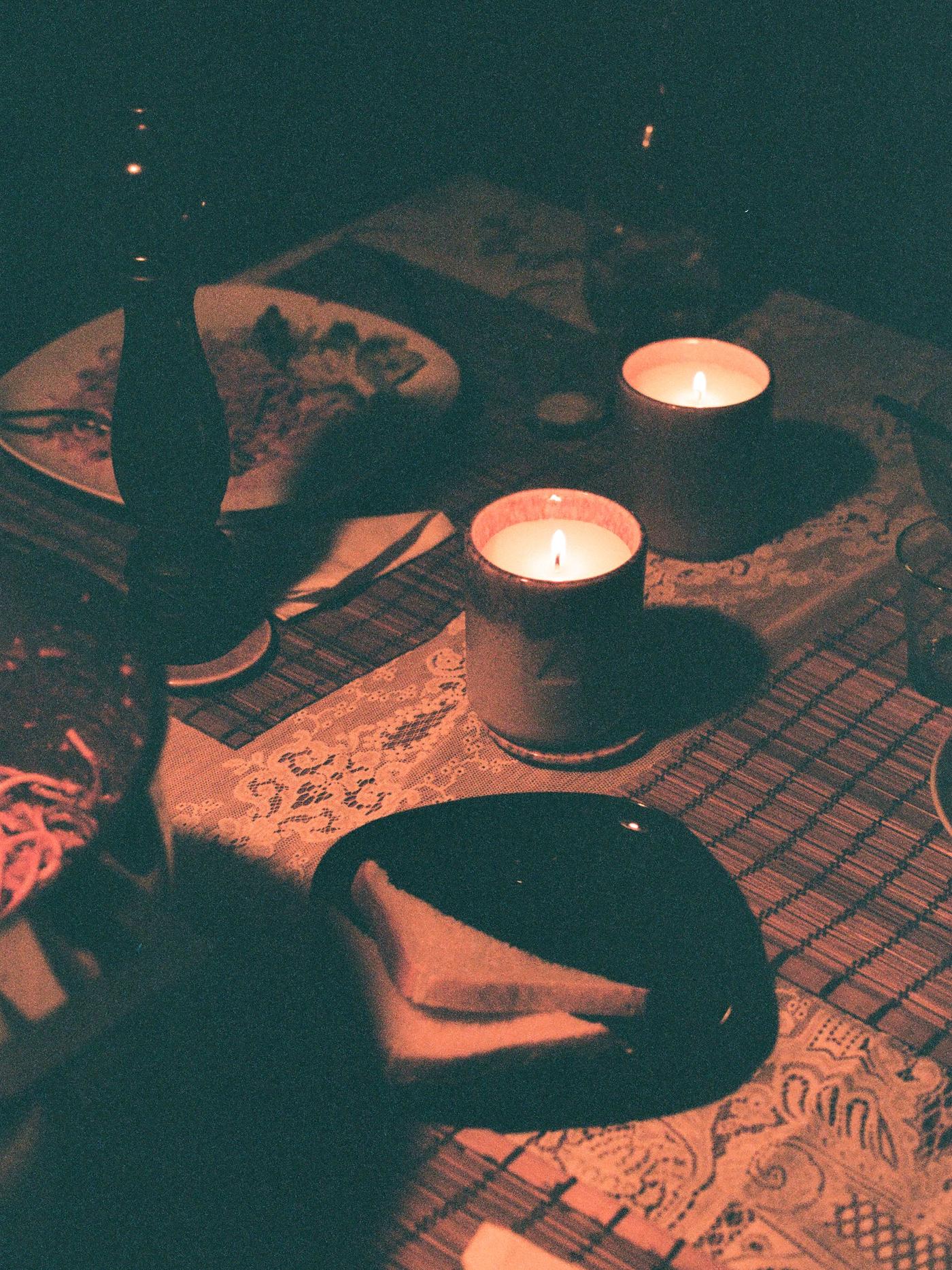 Two burning candles sit on a table, next to a plate with two slices of bread.