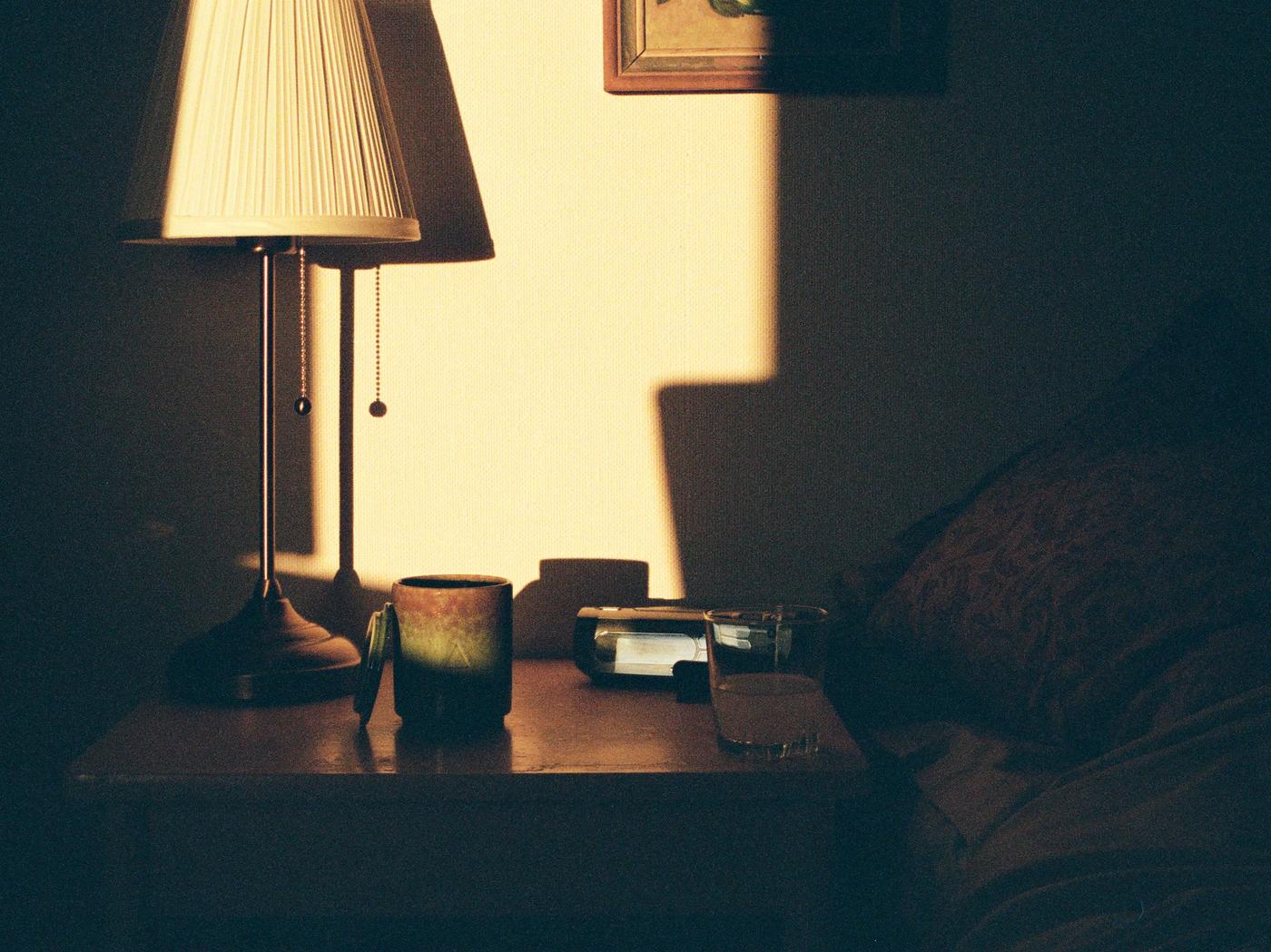 A room with a standing lamp in the corner. On the table is a ceramic candle. The room is dark, wth a little sunlight.