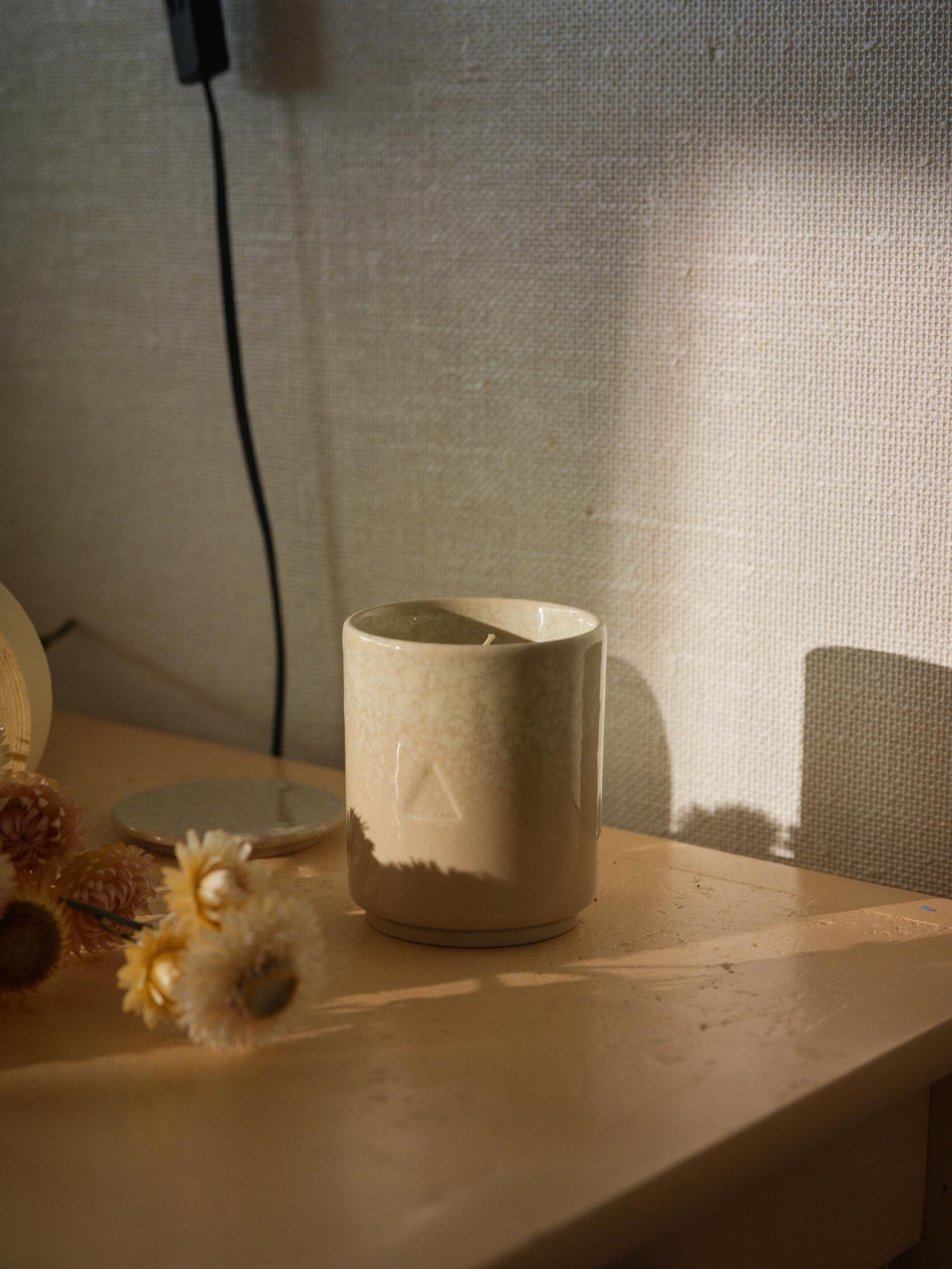 A beige ceramic candle sits on a table next to small lights. There are shadows.