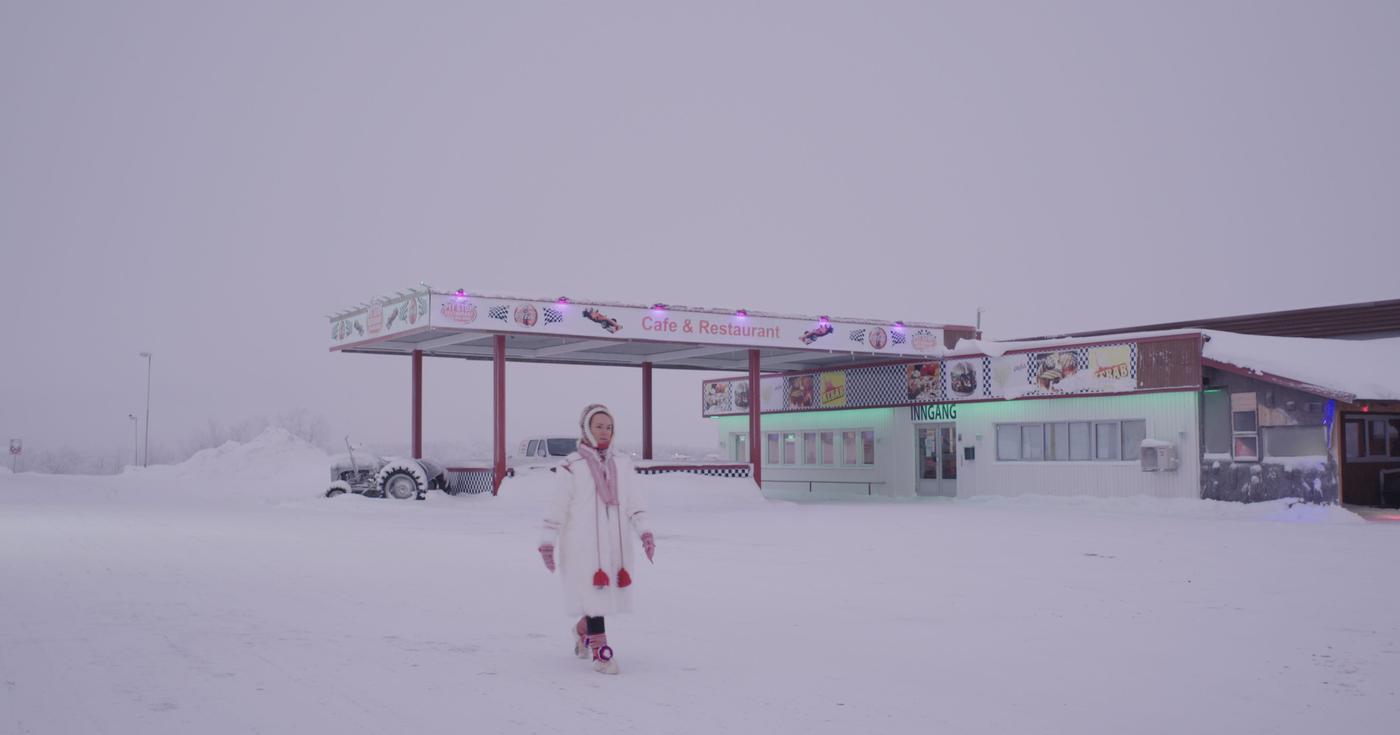A person walks through the snow, past a roadside cafe and restaurant. The person is wearing winter clothes.