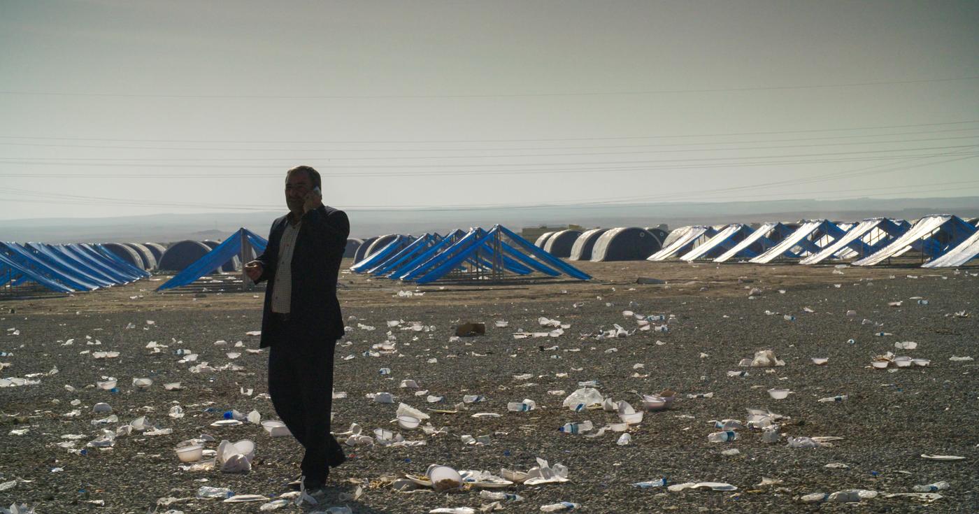 A person stands in a field with rows of tents behind.