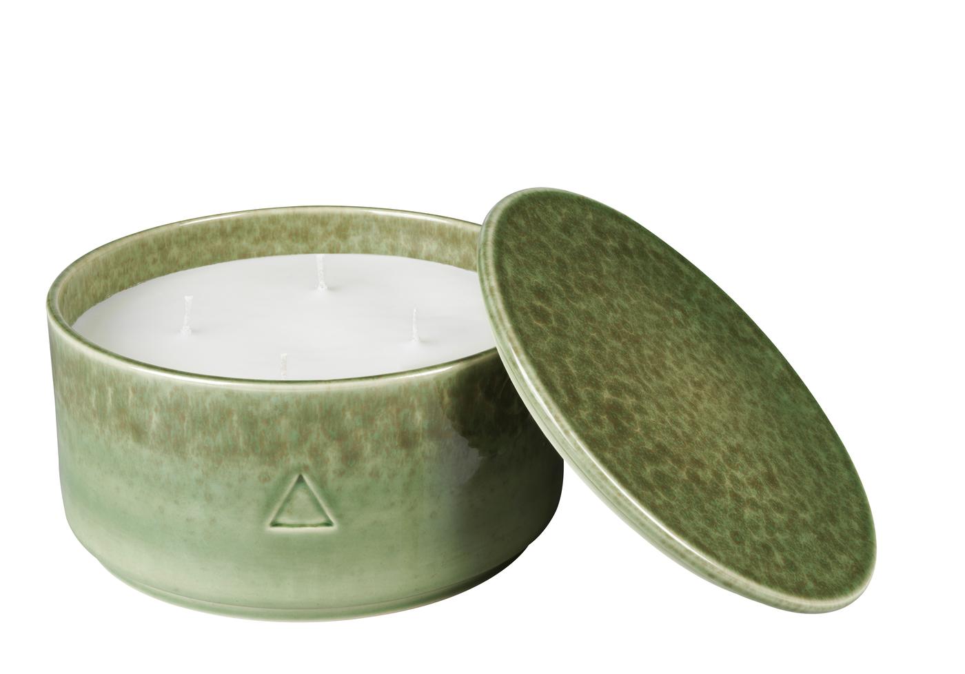 A green ceramic handle holder with a candle inside. Against a white background.