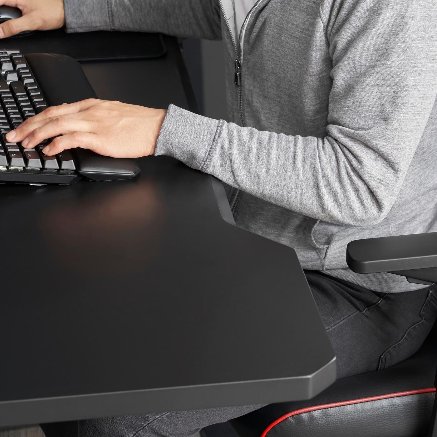 A person wearing a grey zip up hoodie sets at a black desk. Their hands are on a black keyboard.