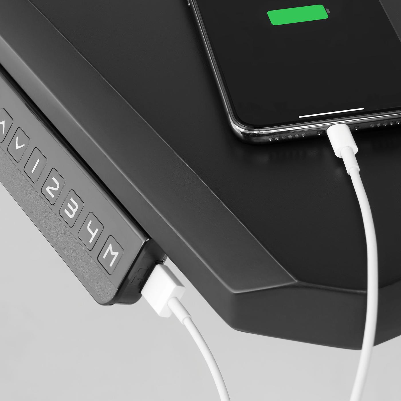 A black phone is connected to a back gaming desk via a white charging cable. 