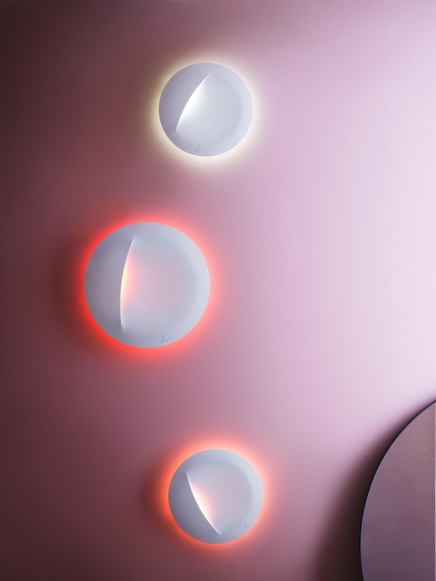 Three illuminated white lamps hang on a pink wall. One has a white light, the others are red and orange.