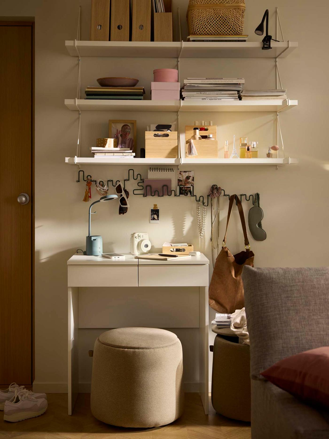 A small vanity area with a white desk and matching shelves above. A round cushioned stool with hidden storage sits in front of the desk.