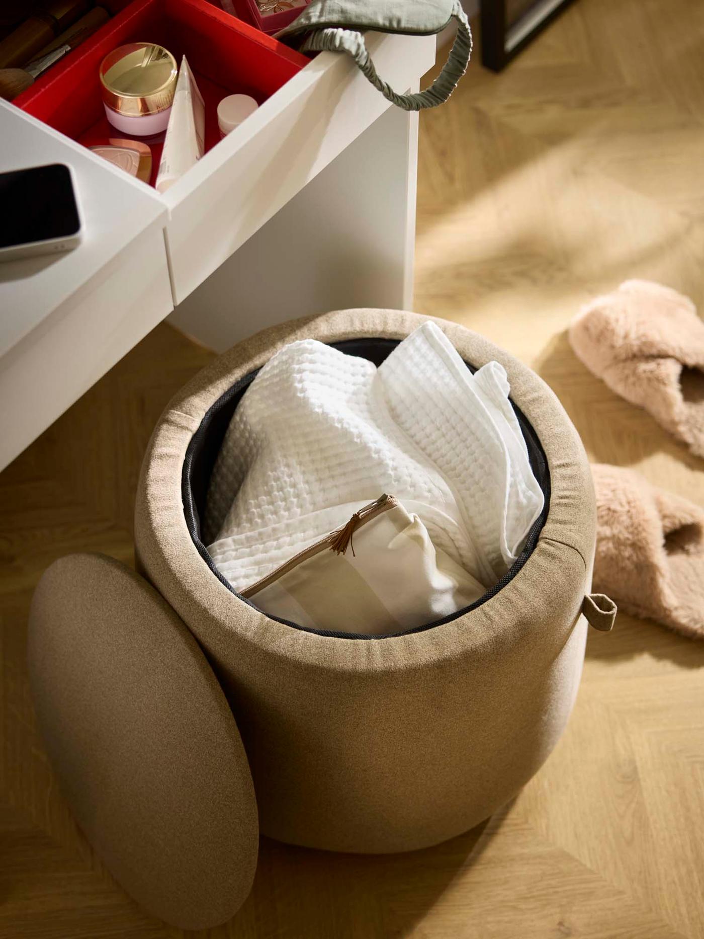 A round cushioned storage stool with its lid removed, revealing textiles stored inside.
