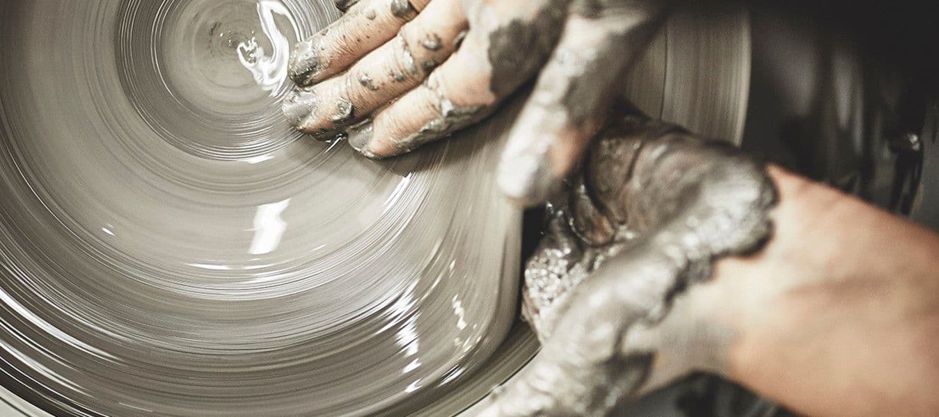 A pair of hands forming a bowl in clay on a turntable.