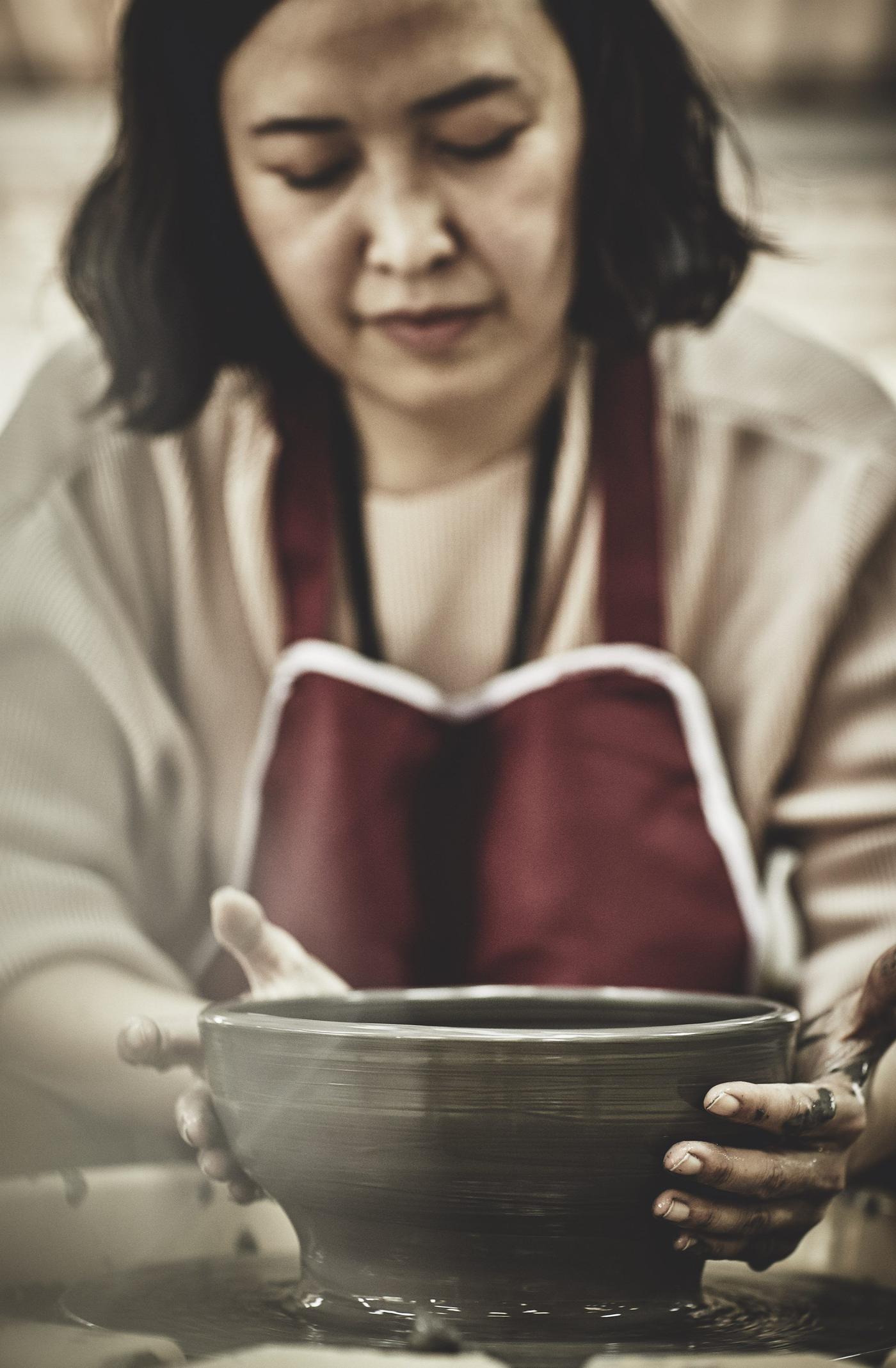 A woman in an apron forming a clay bowl on a turntable.