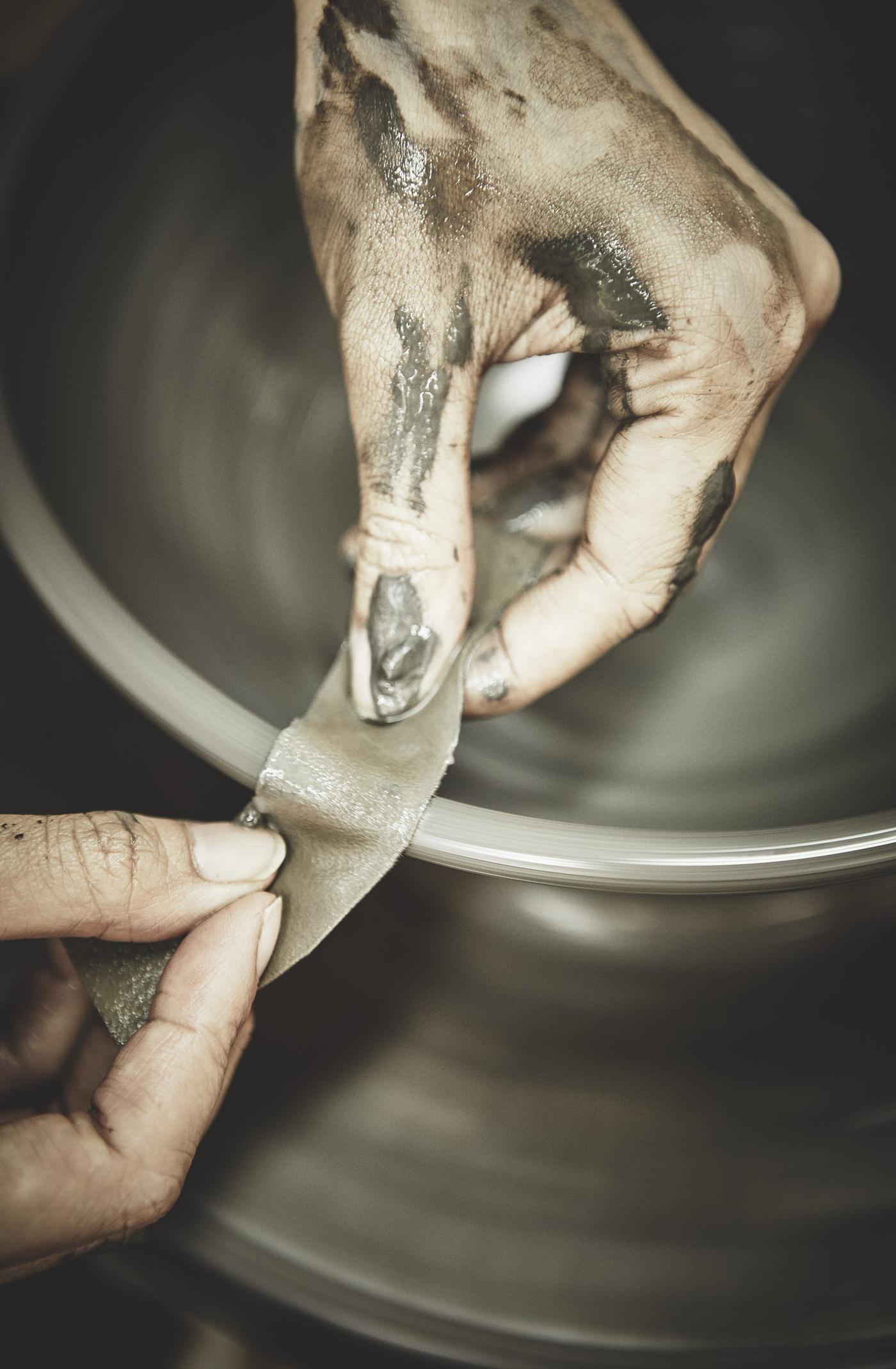 A pair of hands forming a clay bowl on a turntable with a piece of fabric.