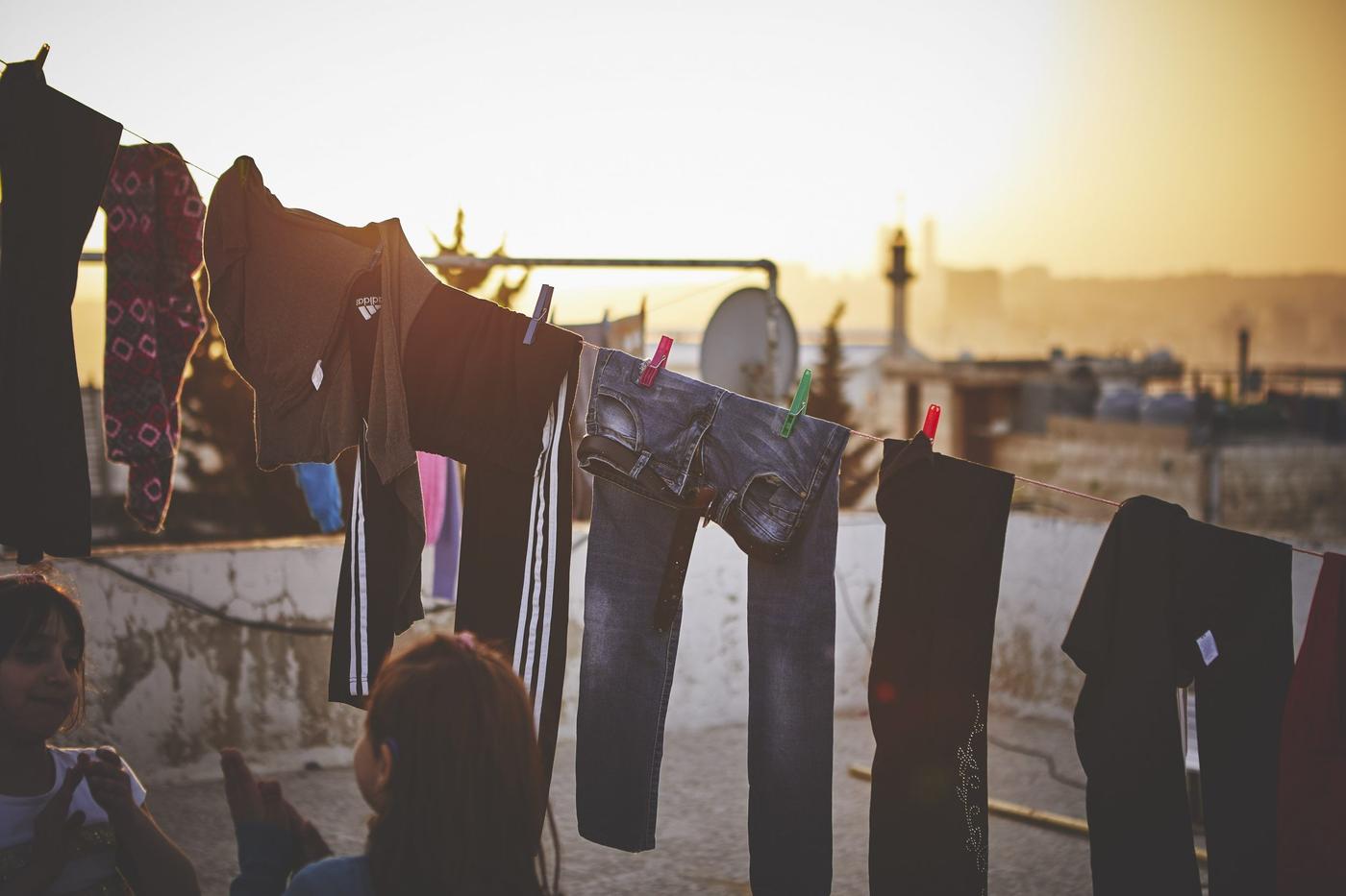 Two children playing in front of various clothes hanging to dry outside on a rooftop.