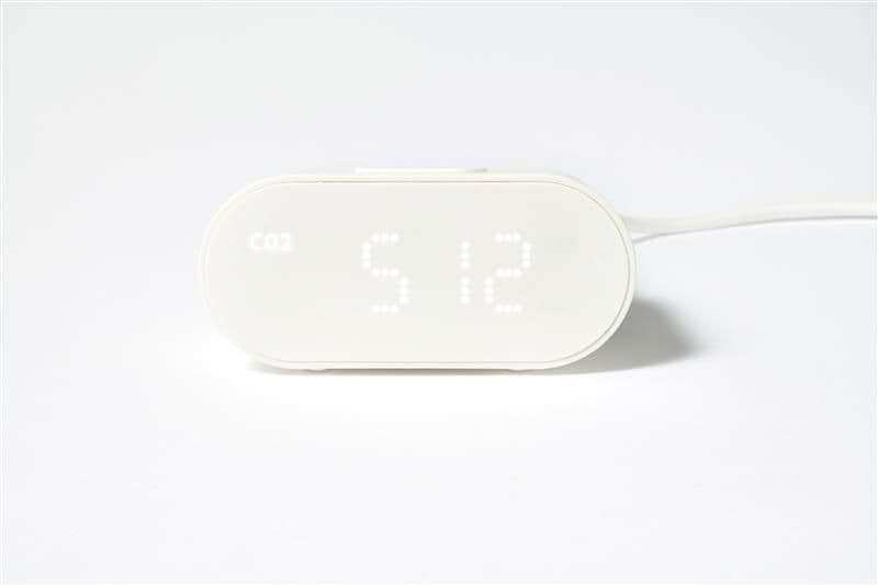 A white sensor with display and side cord against a white background, showing the time.