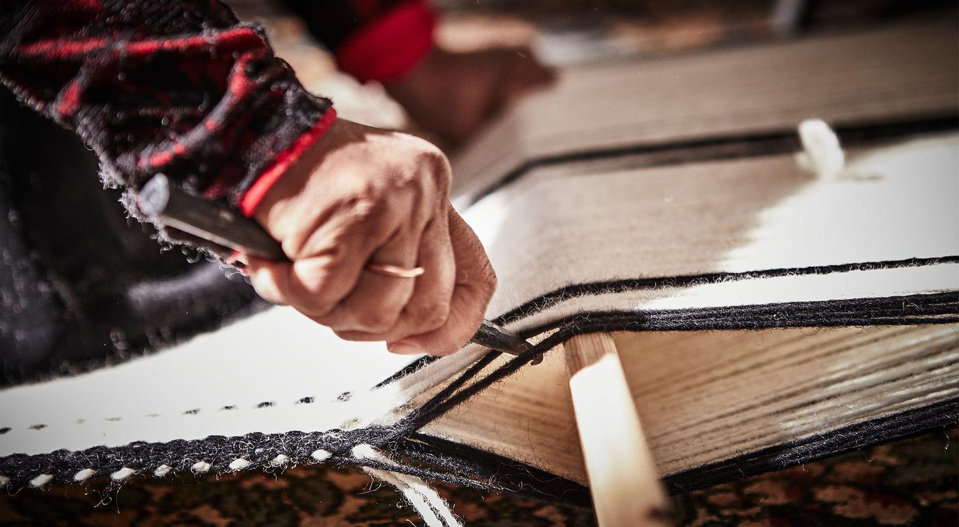 Close up of the hands of an artisan weaving a rug.