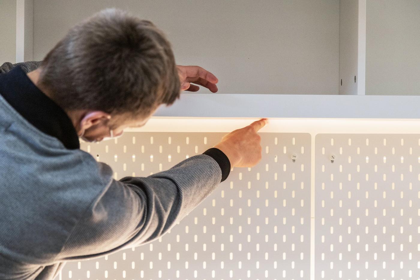 A man with his back towards the camera pointing at a detail on a shelf.