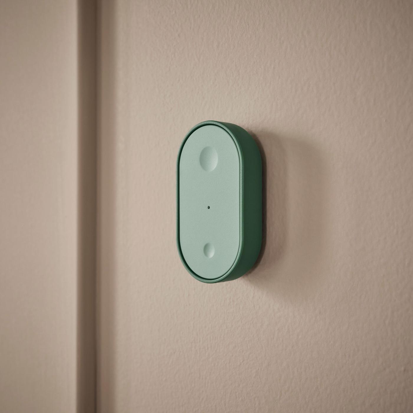 A small green remote with two buttons mounted on a brown-beige wall.