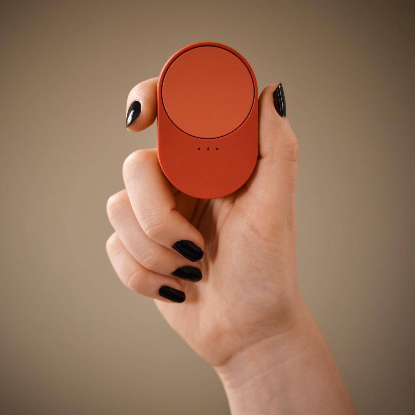 Red remote held between thumb and index finger, with dark nail polish and other fingers visible below.