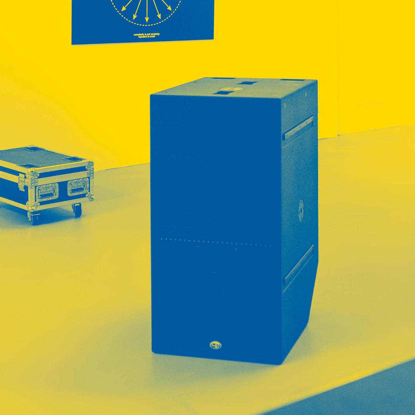 A large speaker on a stage with a case on wheels in the background.