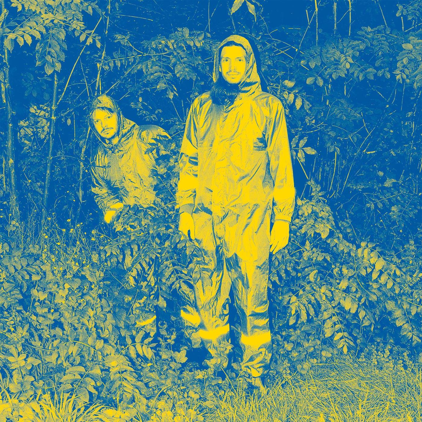 Two people from Public Possession standing in a forest wearing overalls.