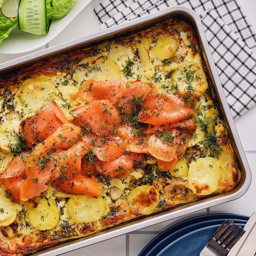 A white dish of smoked salmon and potato bake rests on a white tablecloth, ready to be served.