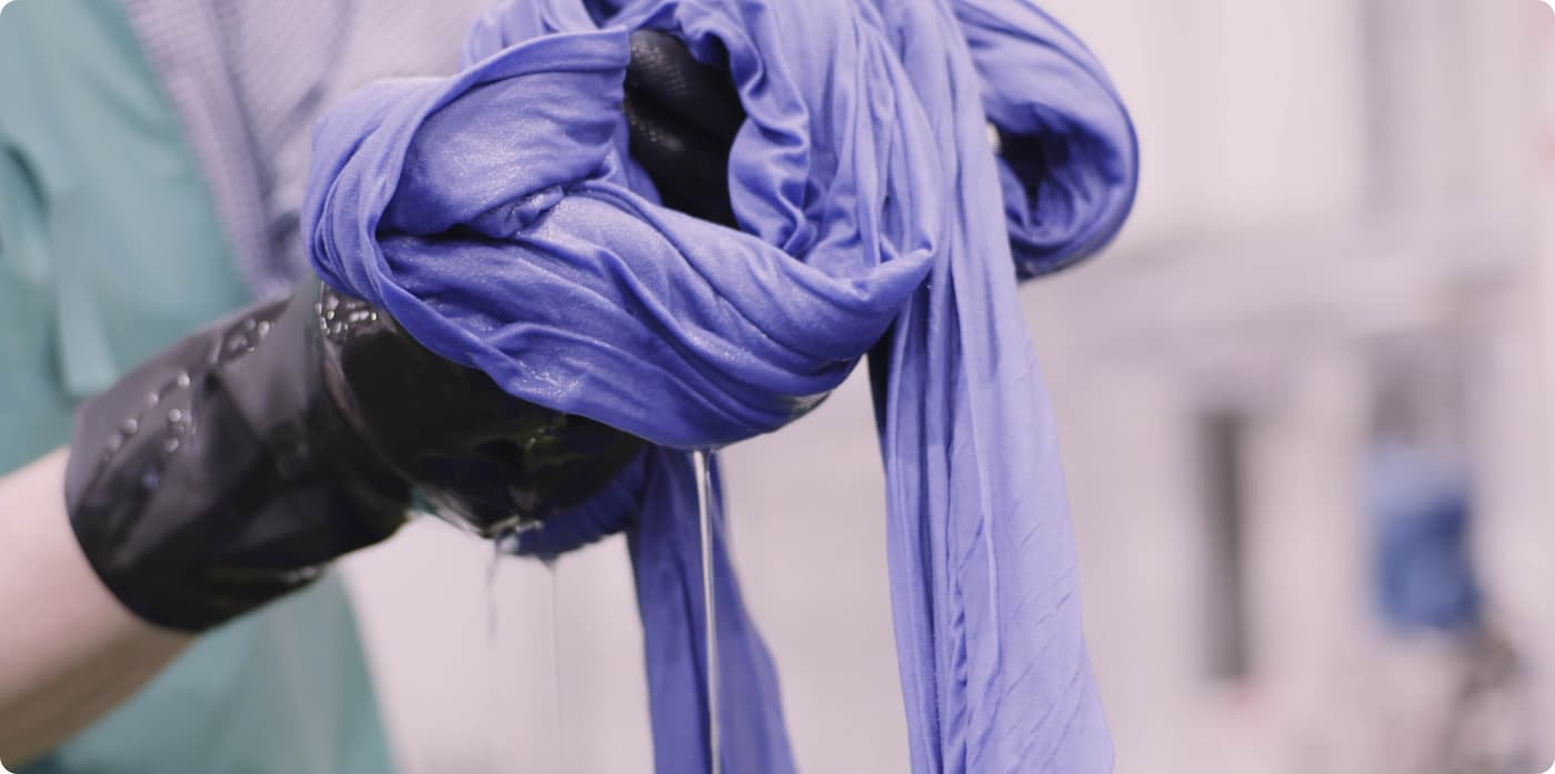 Gloved hands ringing out a wet length of purple fabric.