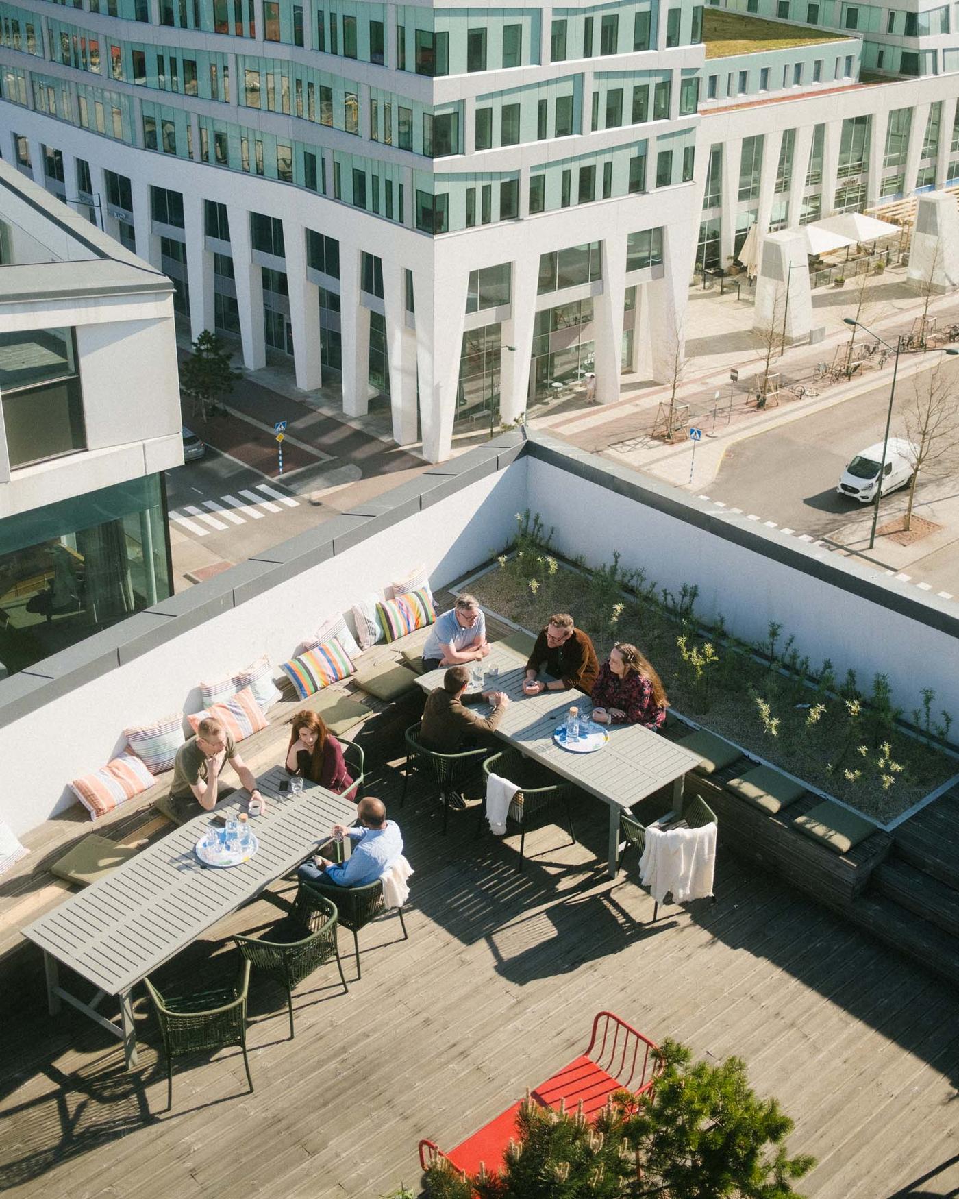 People sit at two tables on rooftop terrace in the sunshine.