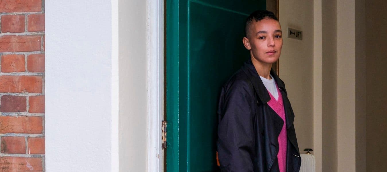 A woman in a blue jacket and pink shirt standing in front of a door.