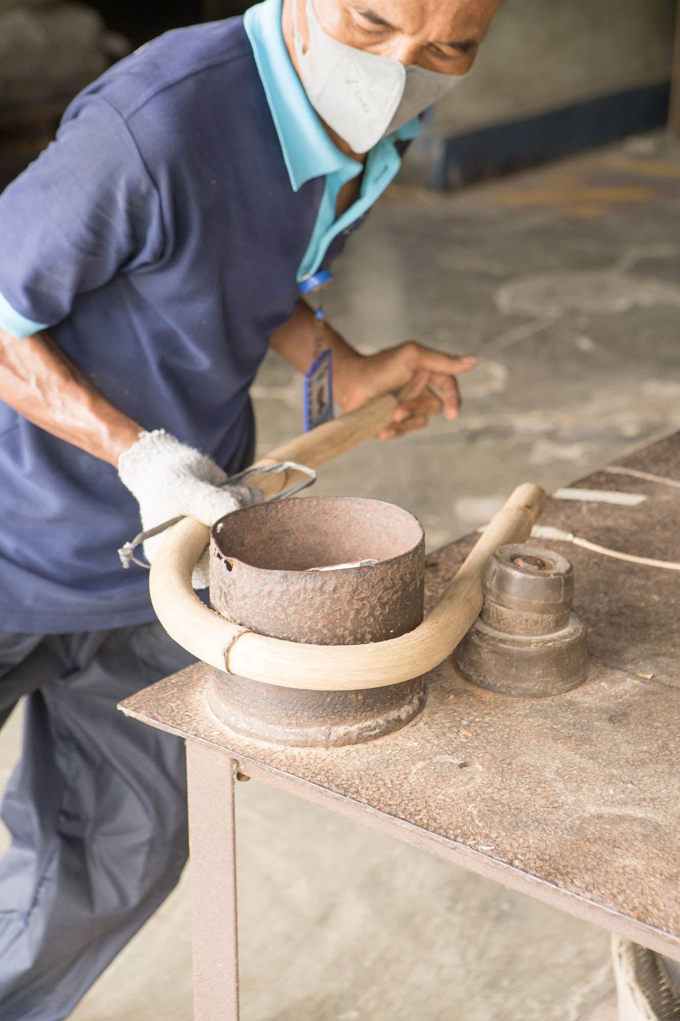 An artisan bends a piece of rattan into shape around a metal mould.