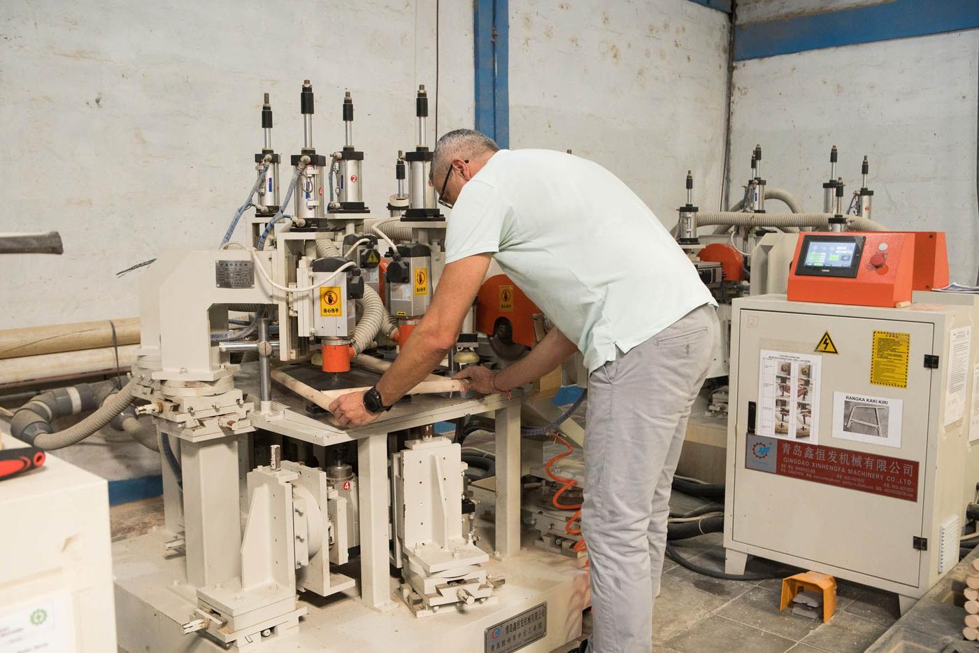 A person bends over a piece of machinery in a manufacturing facility.