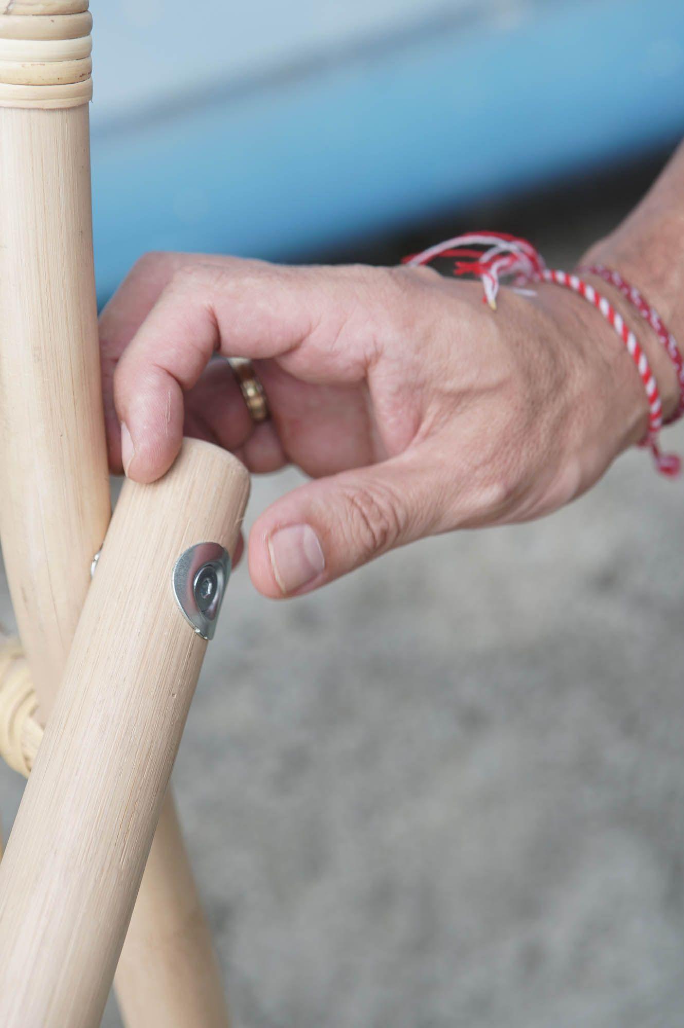 Hands touching the joint of a rattan chair frame, secured with a metal screw.