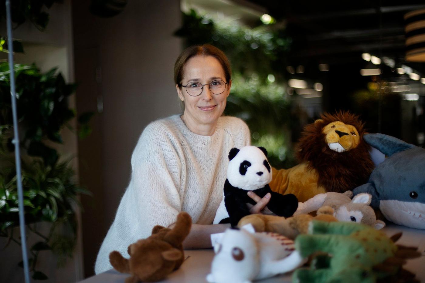 A woman in glasses standing at a table full of soft toys.