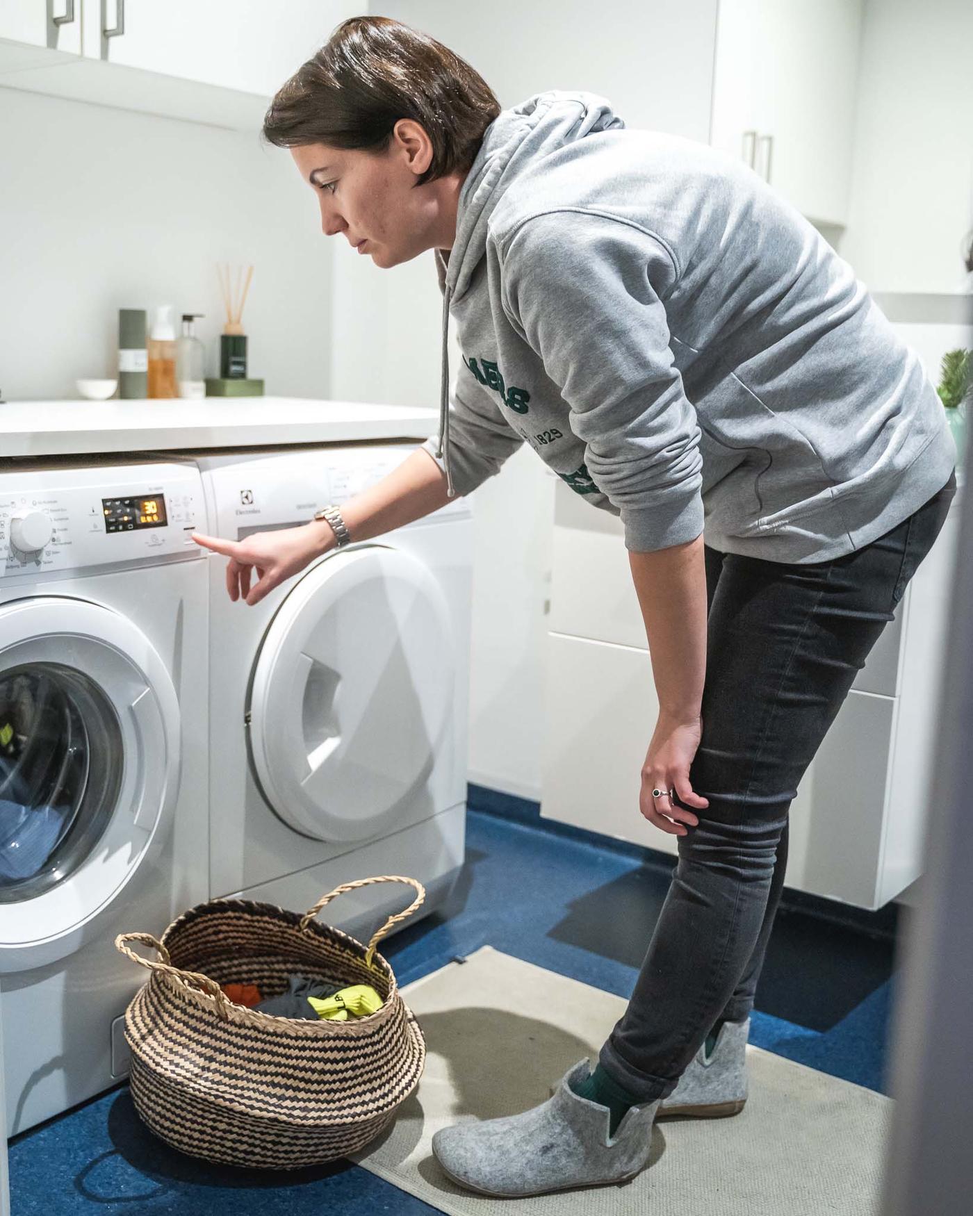 A participant from the Drop it project putting on a load of laundry in a white and blue laundry room.
