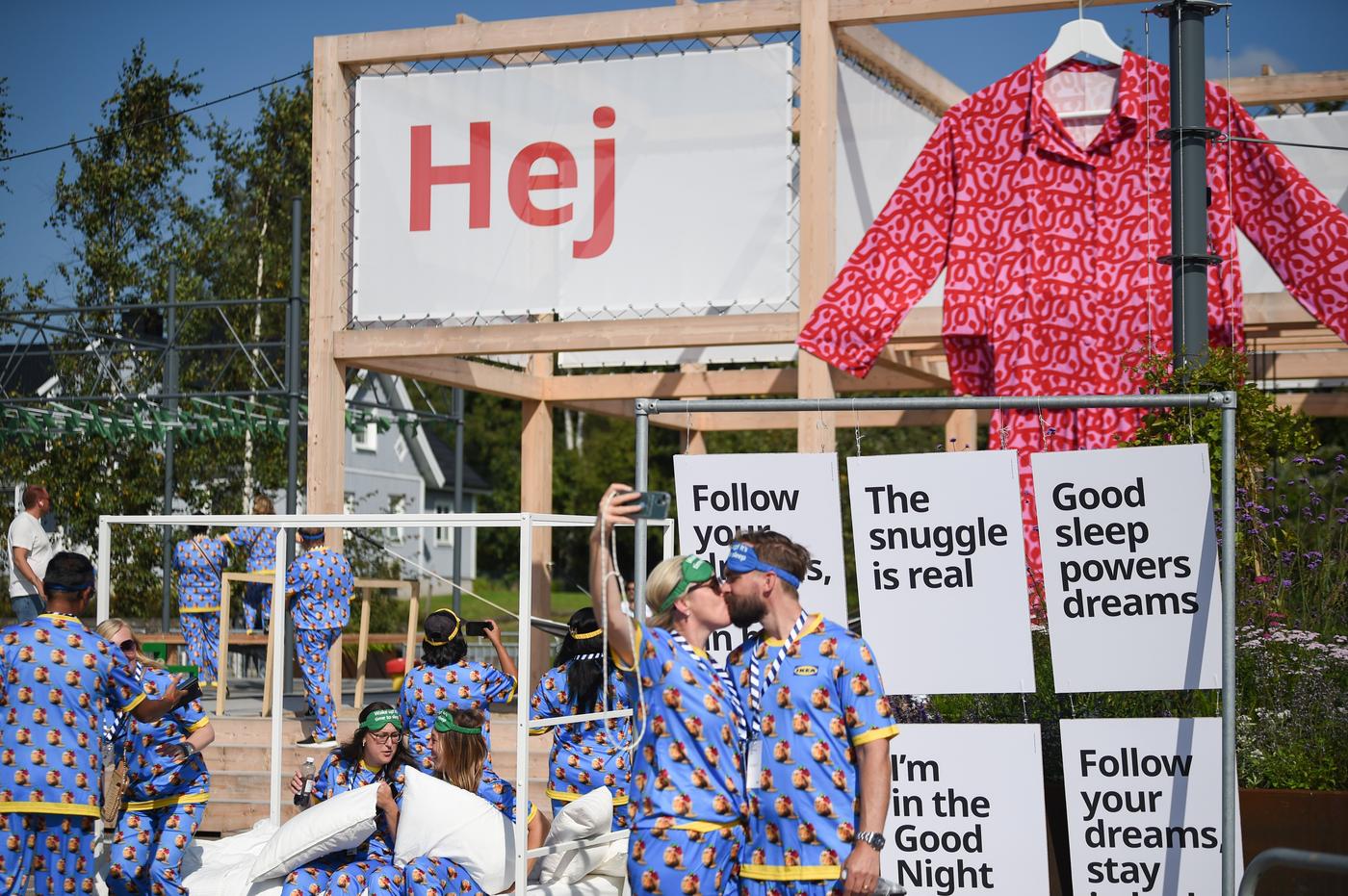 Two people kissing in front of a big sign saying "Hej"
