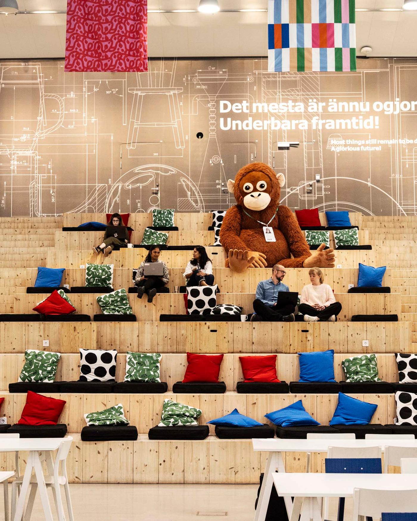 Colleagues sitting together and chatting on deep, pine stairs with IKEA cushions in an auditorium-like space.