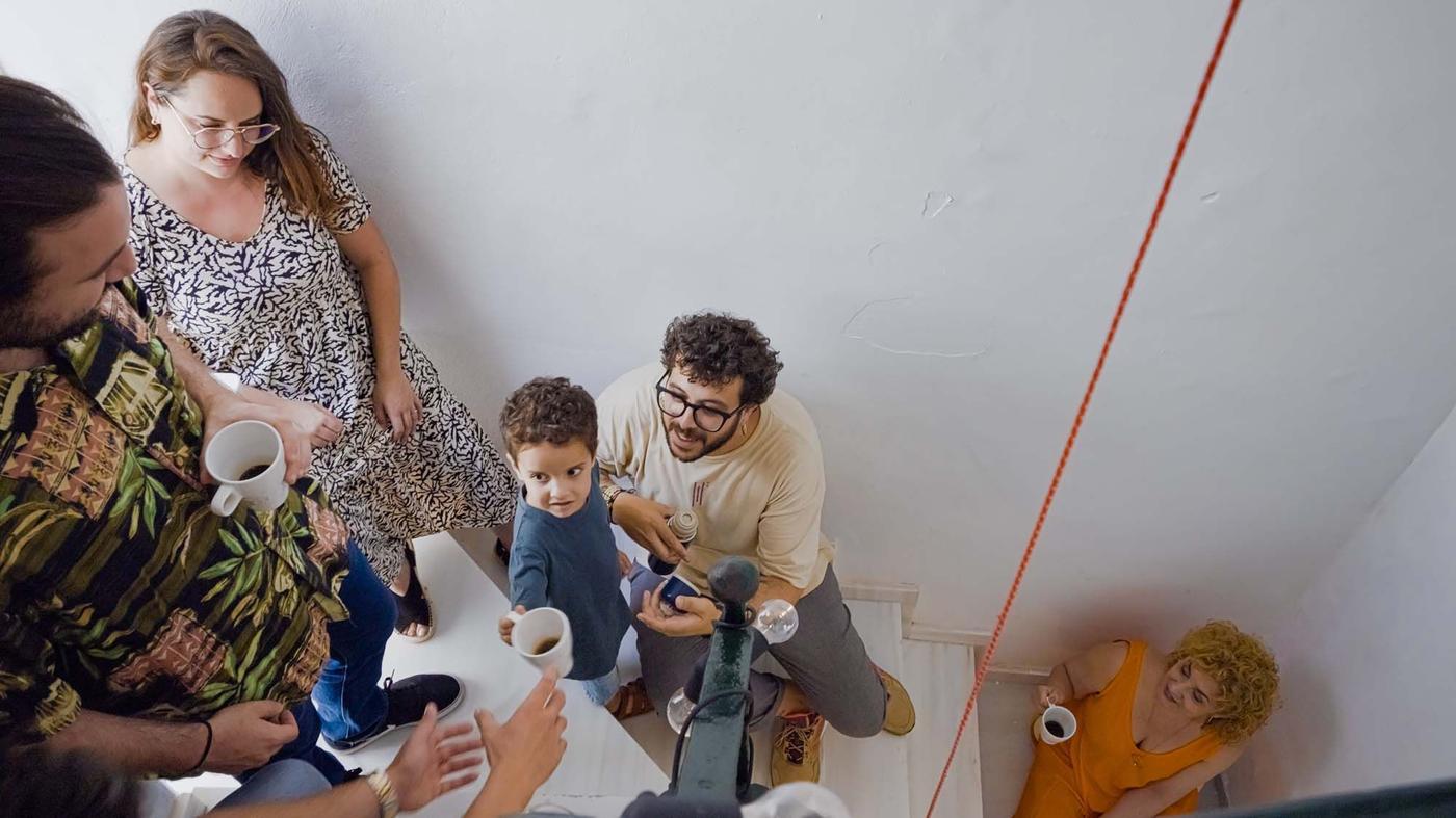 A group of neighbours sit on the stairway drinking coffee, eating cake and chatting.