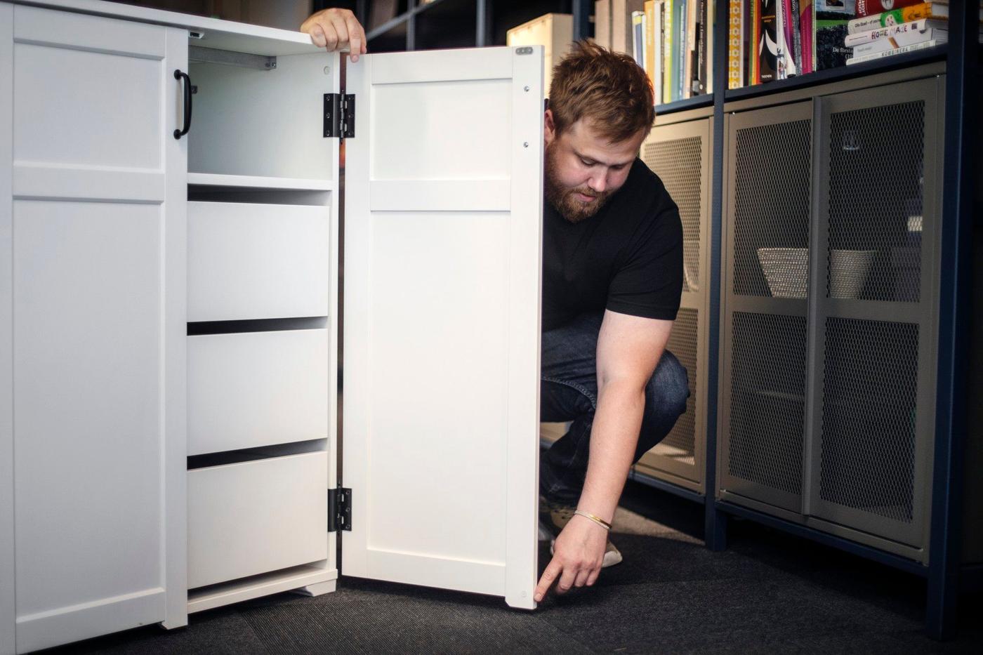 A man pointing towards the bottom of a door of a white cabinet.