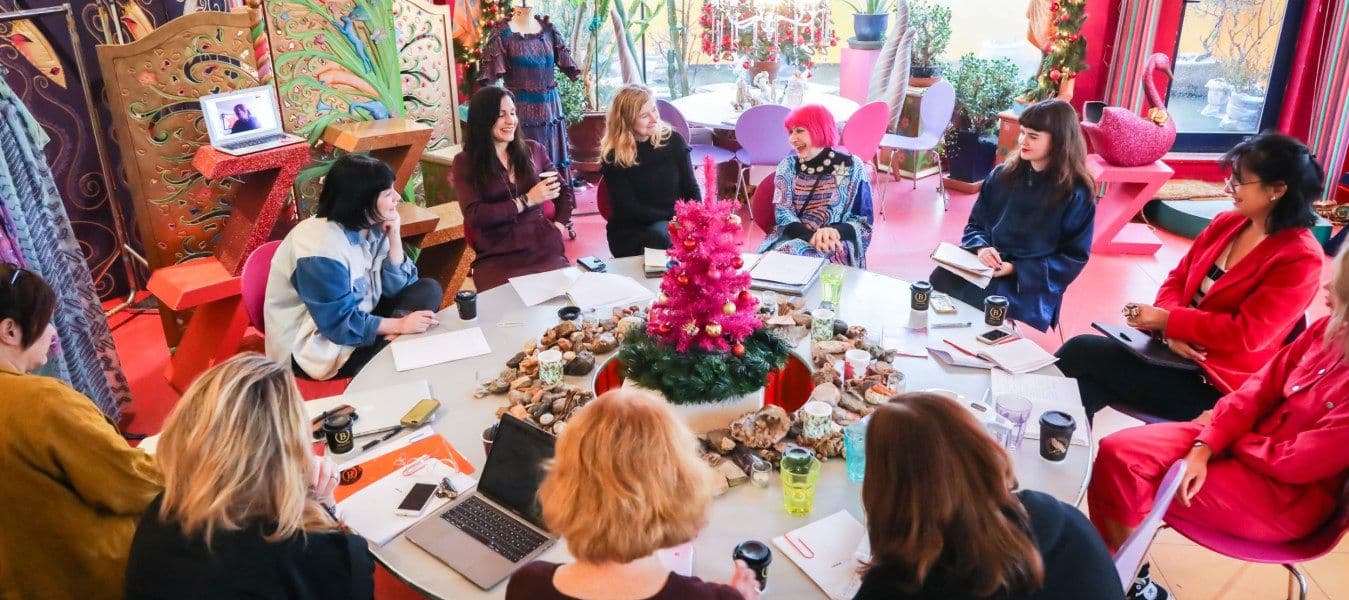 A colourful room with a large, round table with eleven women having a meeting around it.
