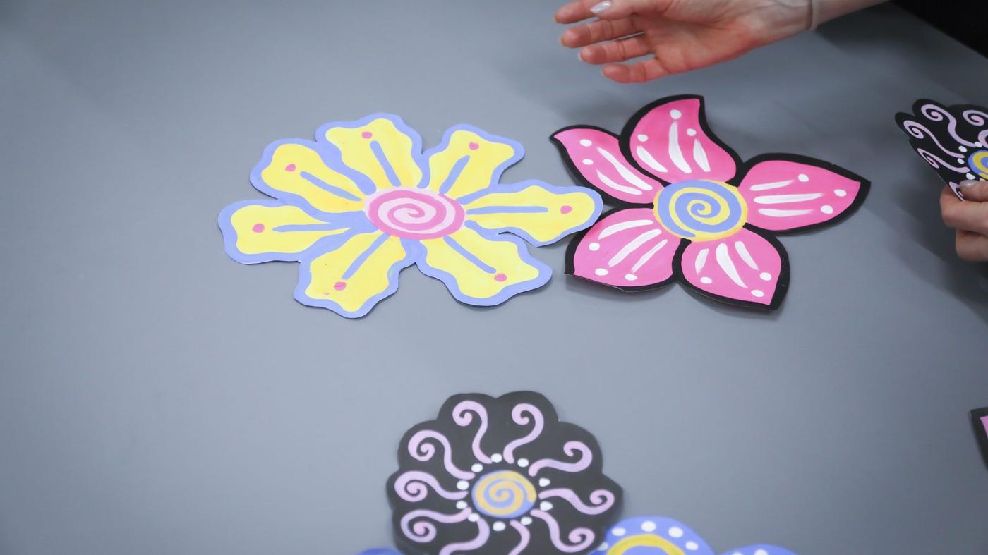 A pair of hands placing cut-out flower prints in different colours on a grey tabletop.