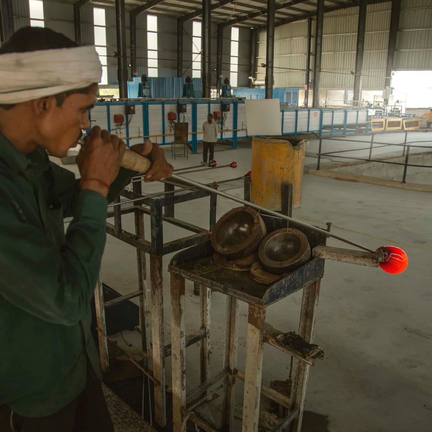 A person blows through a metal pipe to create a glass vase.