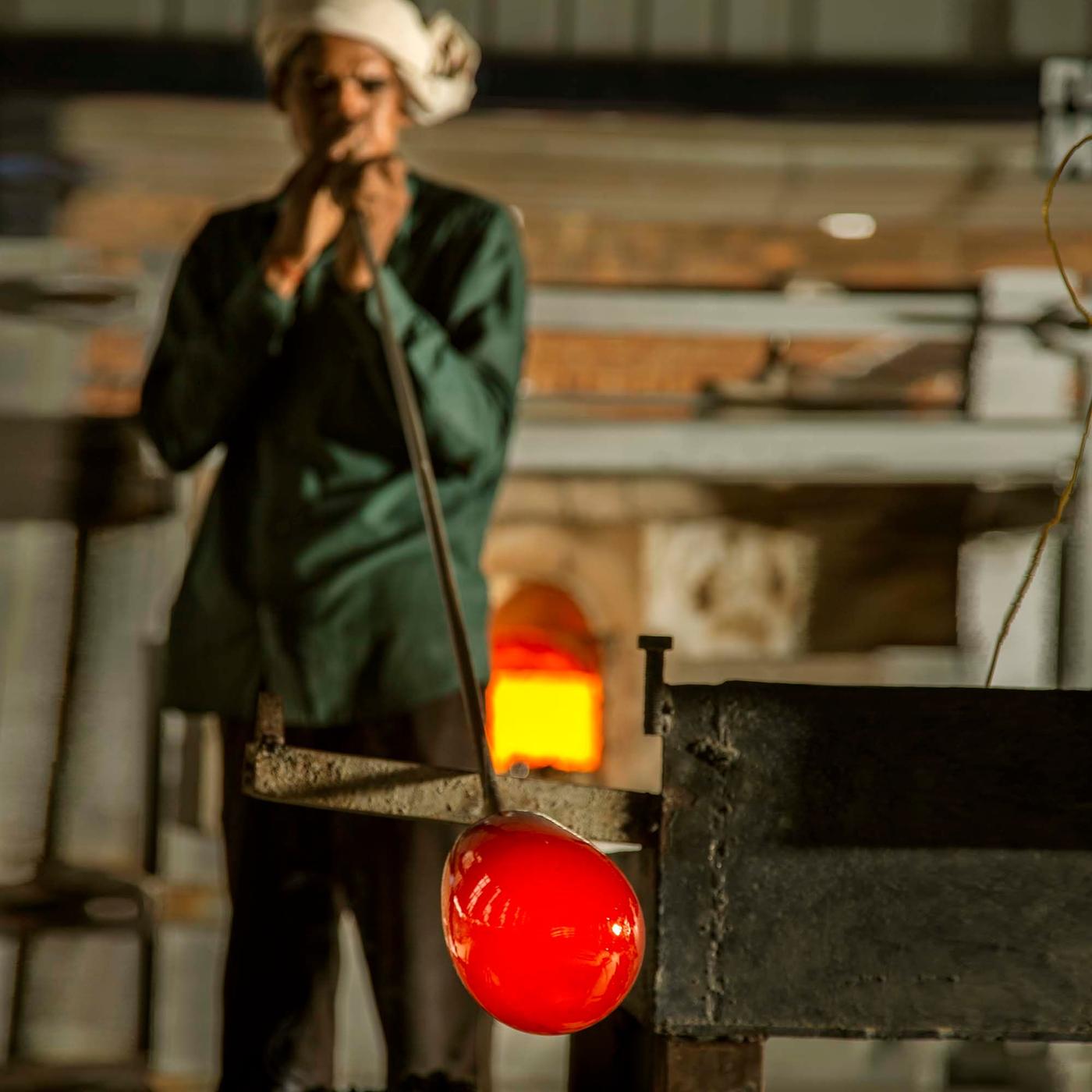 A person blows a glass HANGBJÖRK vase through a metal pipe.