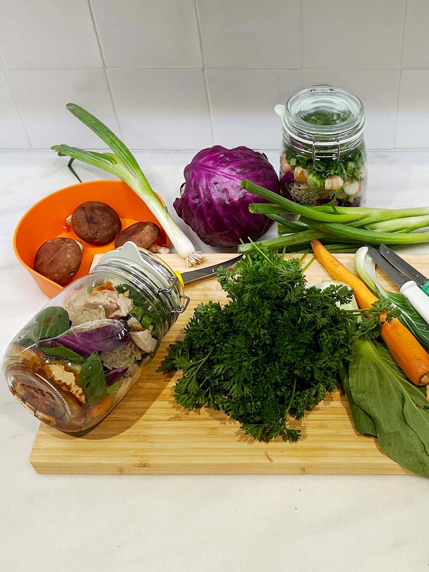 An array of ingredients, including carrots, leeks, cabbage and herbs on a chopping board.