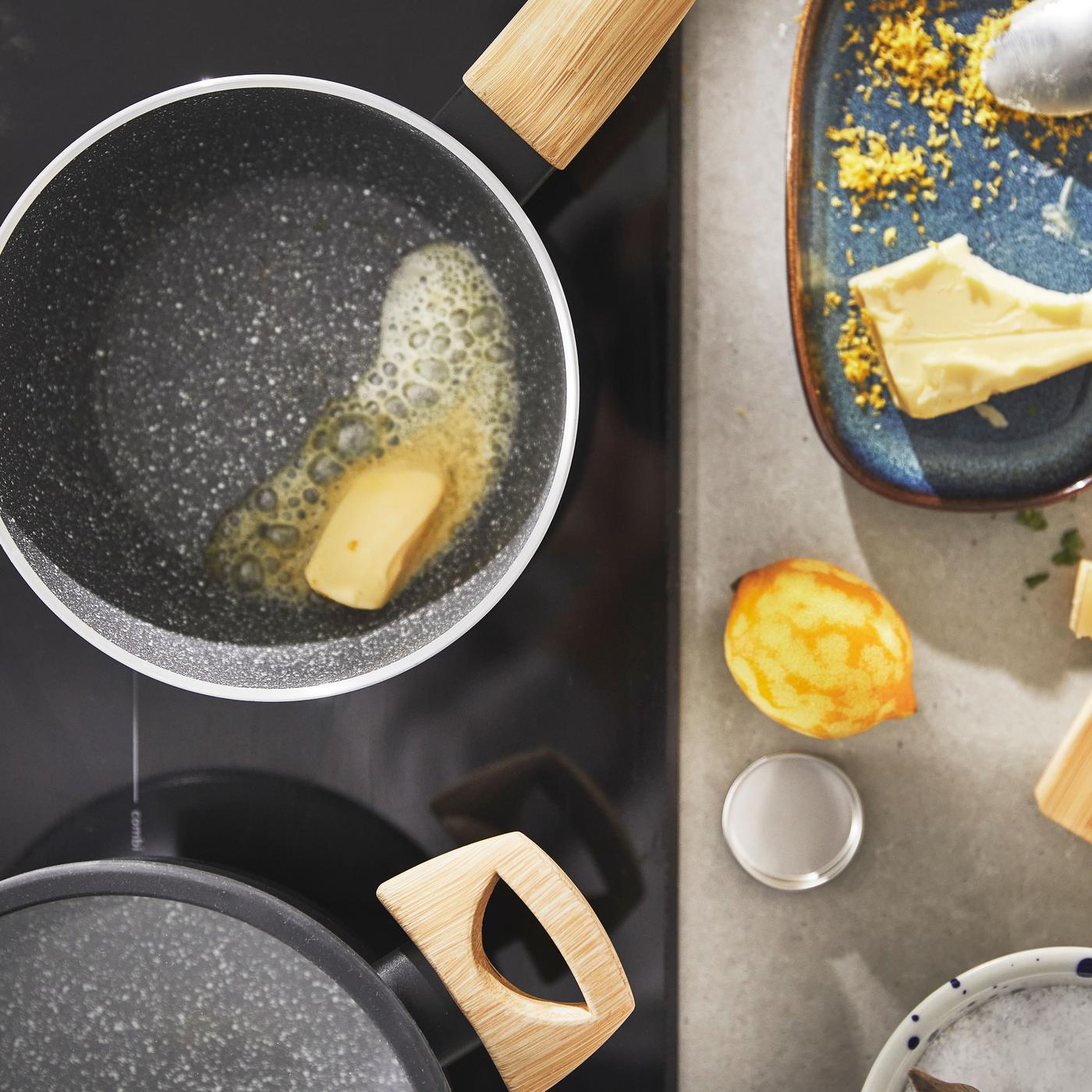 The HUSKNUT pan with some melting butter in it. On the side a plate with some rasped lemon and butter on it and a lemon who's skin has been rasped.