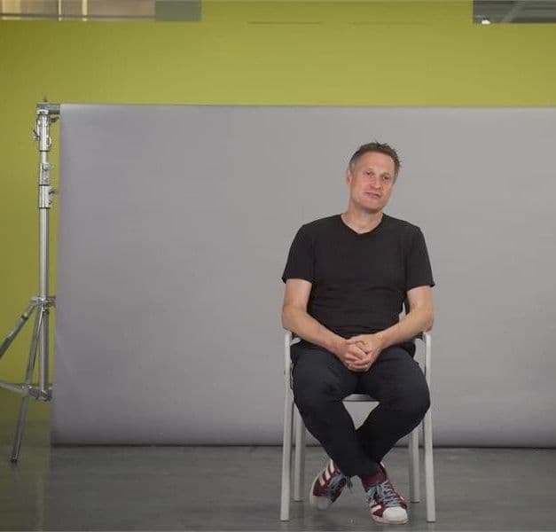Person seated in a chair in front of a grey backdrop.