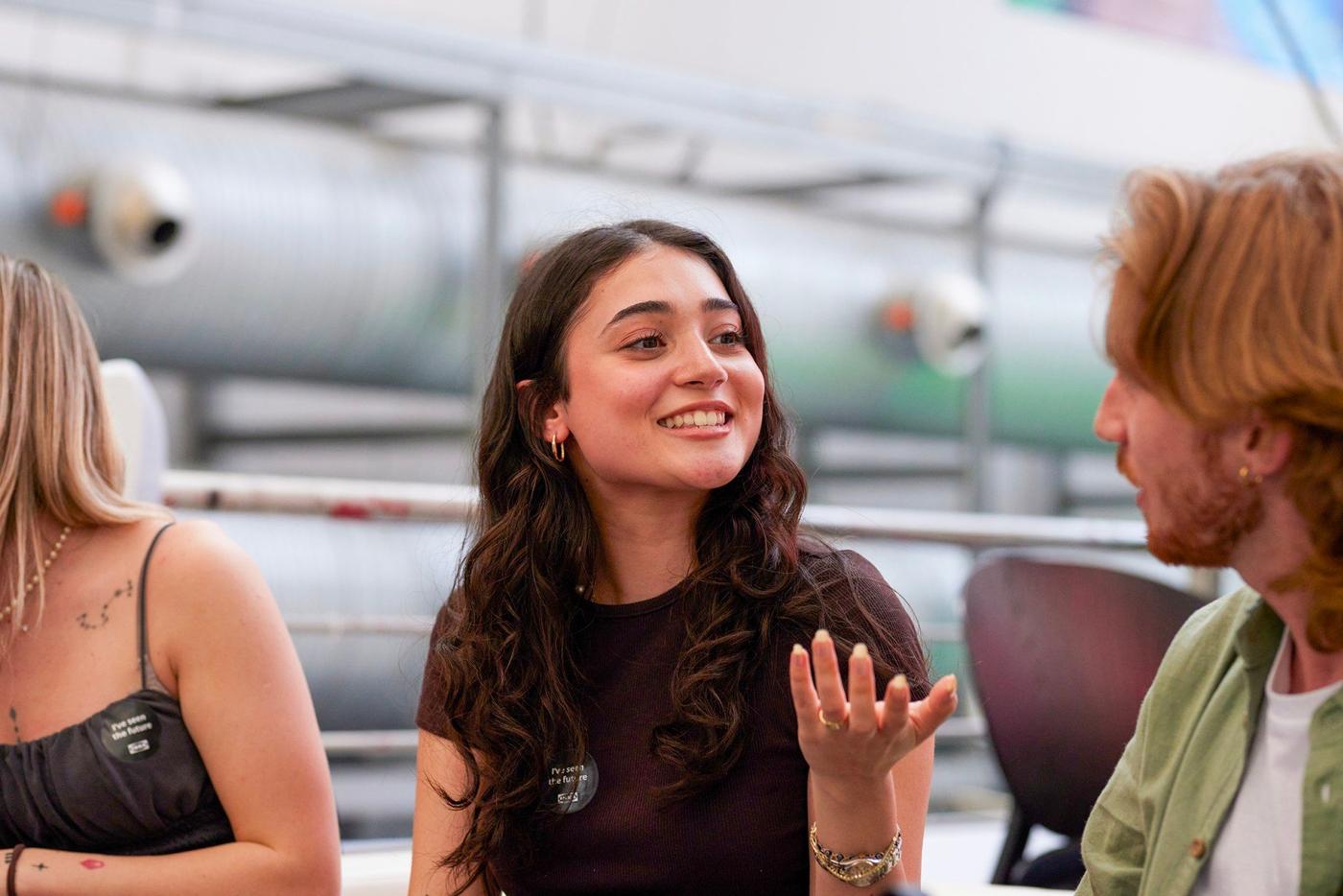 A woman in a black dress sitting in a conversation with another person, gesturing.