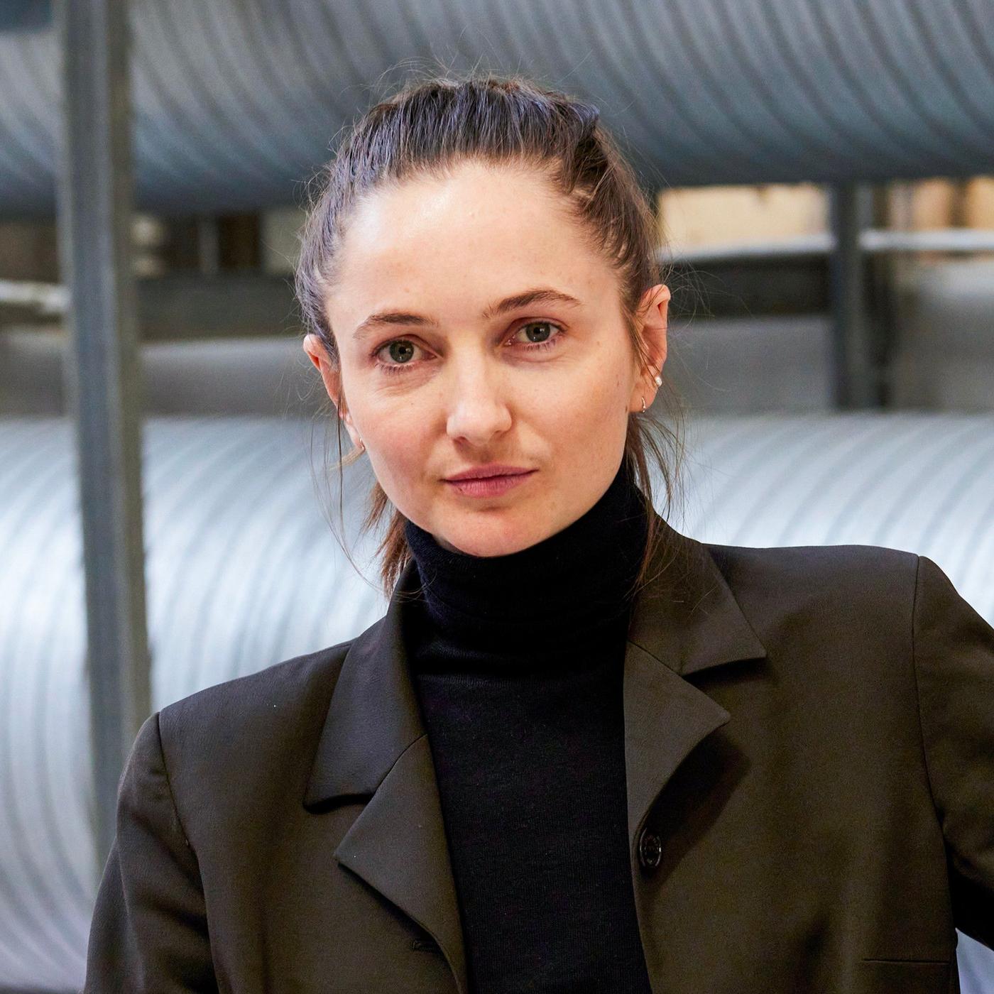 A portrait of a dark haired woman in a black jacket and a black turtleneck.