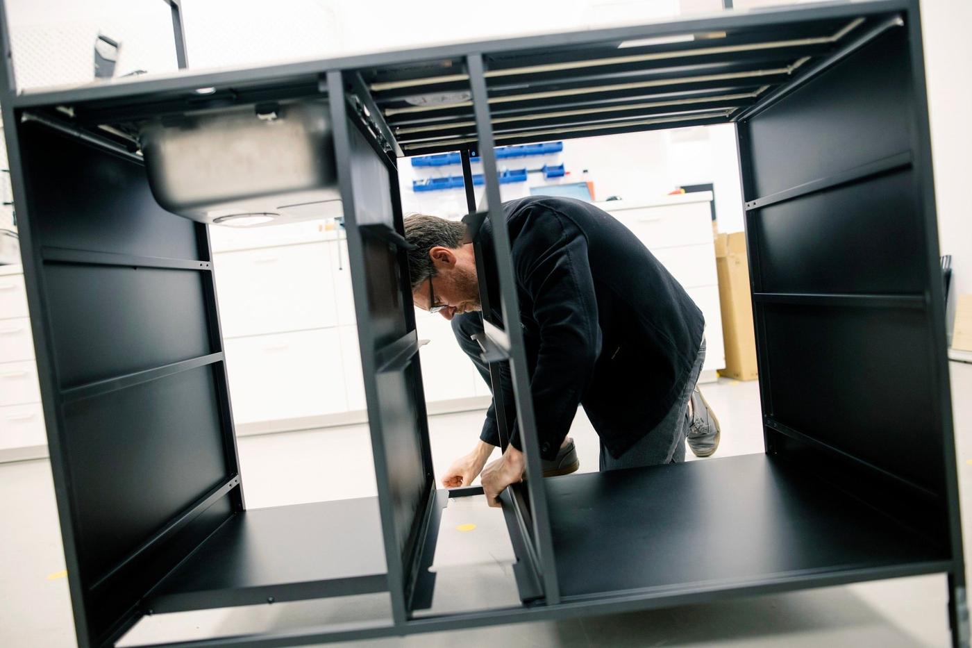 A man lying on his knees assembling an IKEA kitchen.